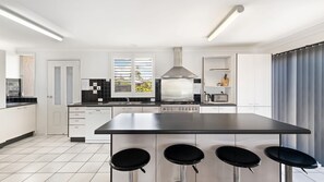 A modern kitchen with a central island, bar stools, and a view of the outdoors through the window.