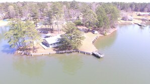 Vue aérienne d’une propriété au bord du lac, avec un quai, une maison et les arbres environnants.