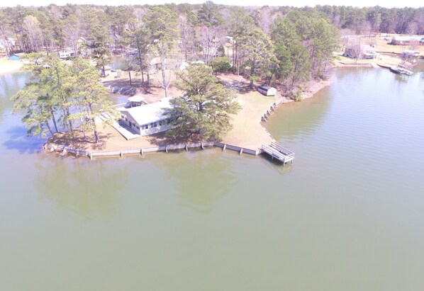 An aerial view of a lakeside property with a dock, a house, and surrounding trees.