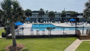 A swimming pool with a fenced deck, lounge chairs, and umbrellas.