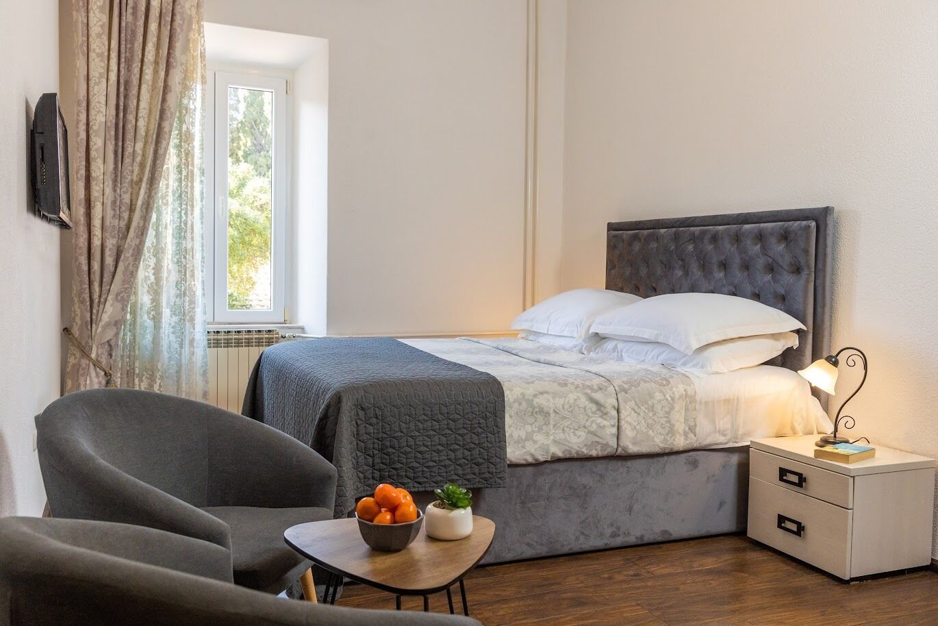 Ein ordentlich eingerichtetes Schlafzimmer mit Bett, Nachttisch, Sessel und einem kleinen Tisch mit Obst.