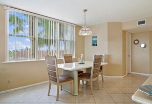 A dining area with a white table and chairs, a hanging light fixture, and a window with blinds.