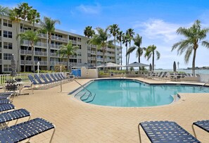 A pool area with lounge chairs and palm trees, surrounded by a multi-story building.