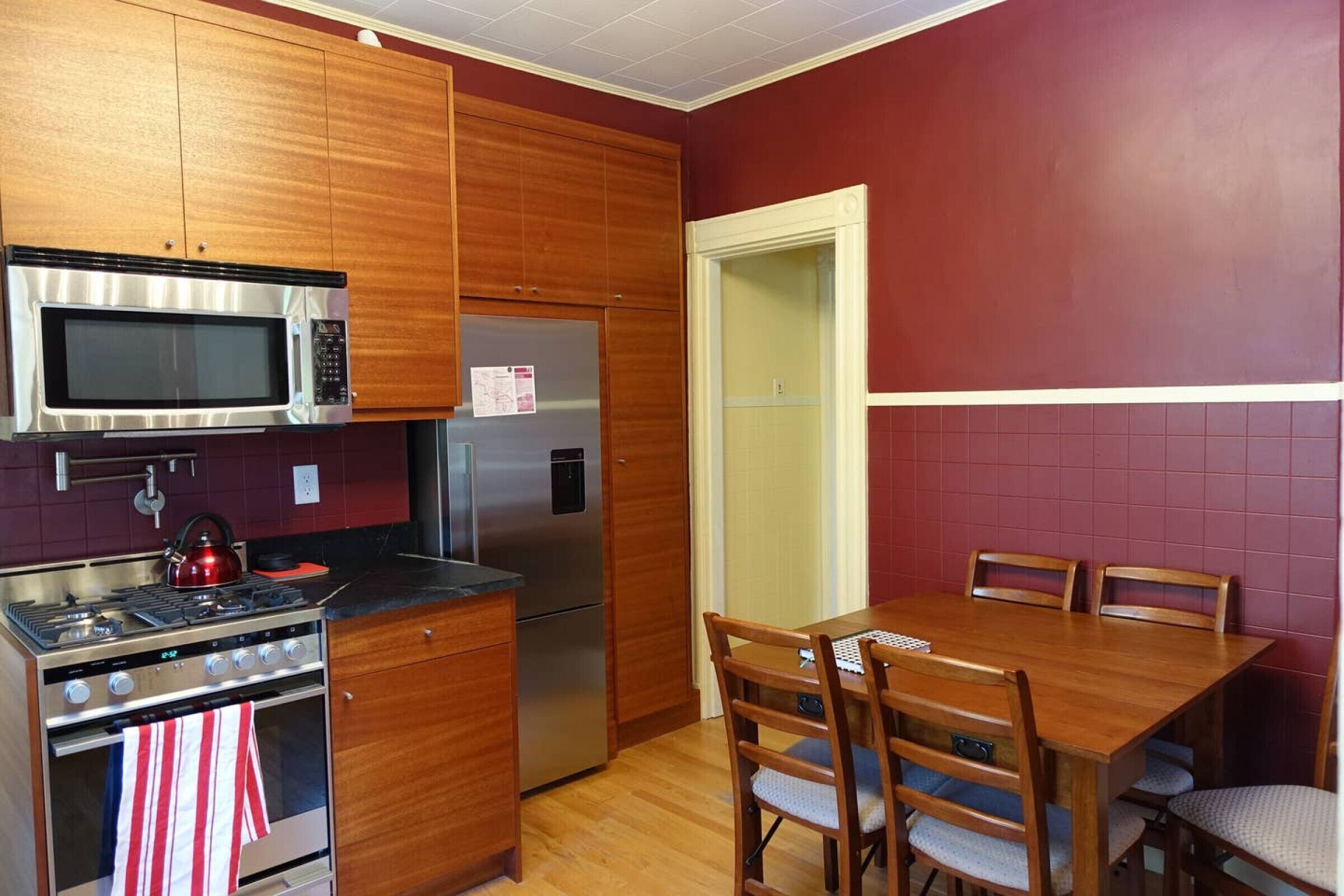 A kitchen with wooden cabinets, a stainless steel microwave, a refrigerator, a stove, and a dining table with chairs.