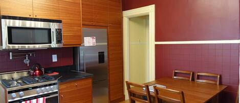 A kitchen with wooden cabinets, a stainless steel microwave, a refrigerator, a stove, and a dining table with chairs.