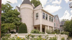 Une maison à deux étages, dotée d’une tourelle, d’un porche et d’une clôture blanche en piquets.