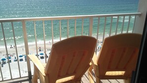 A balcony with two wooden rocking chairs overlooking a beach with people and umbrellas. - The Summit Resort,last min deal, Oct.1-3rd,10% disc. 20% off premisis drink,food (Panama City Beach)