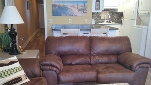 A living room with a brown leather sofa, a wooden coffee table, and a kitchen in the background. - The Summit Resort,last min deal, Oct.1-3rd,10% disc. 20% off premisis drink,food (Panama City Beach)