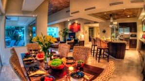A modern dining area with a large table set for a meal, surrounded by wicker chairs, and a kitchen with stainless steel appliances in the background. - Molino de Agua Next to Los Muertos Beach! 3BD Condo for rent in Los Muertos Beac (Puerto Vallarta)