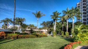 A well-maintained garden with palm trees, red flowers, and a clear blue sky. - Molino de Agua Next to Los Muertos Beach! 3BD Condo for rent in Los Muertos Beac (Puerto Vallarta)