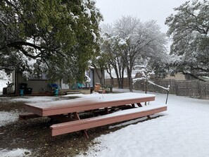 Una mesa de picnic cubierta de nieve, rodeada de árboles y una valla de madera.