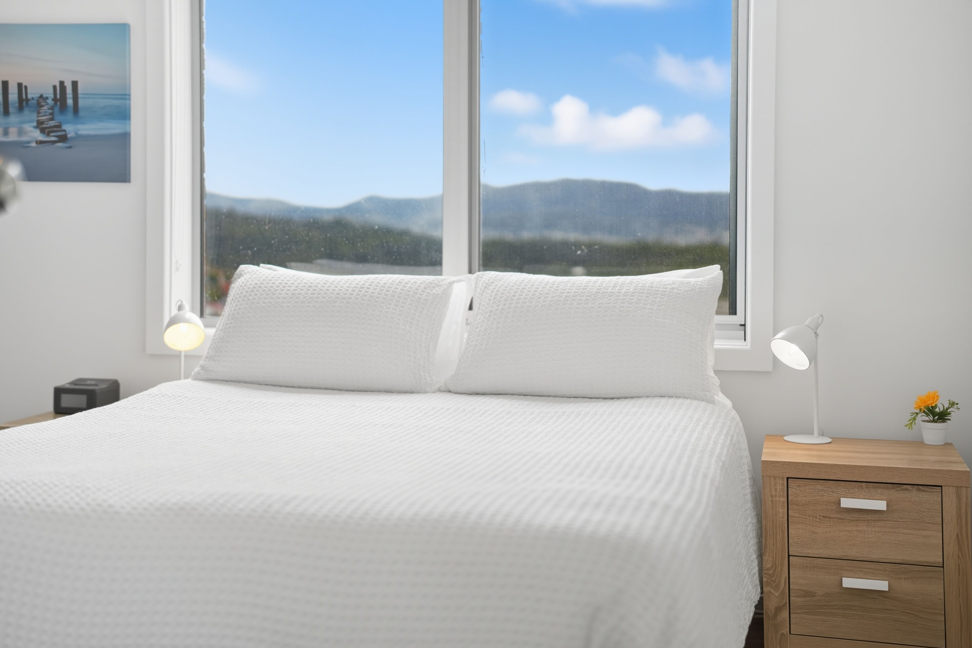 Un dormitorio con una cama, dos lámparas de noche, una mesita de noche con lámpara y una ventana con vistas a las montañas.