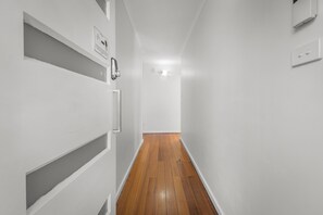 A narrow hallway with white walls and wooden flooring.