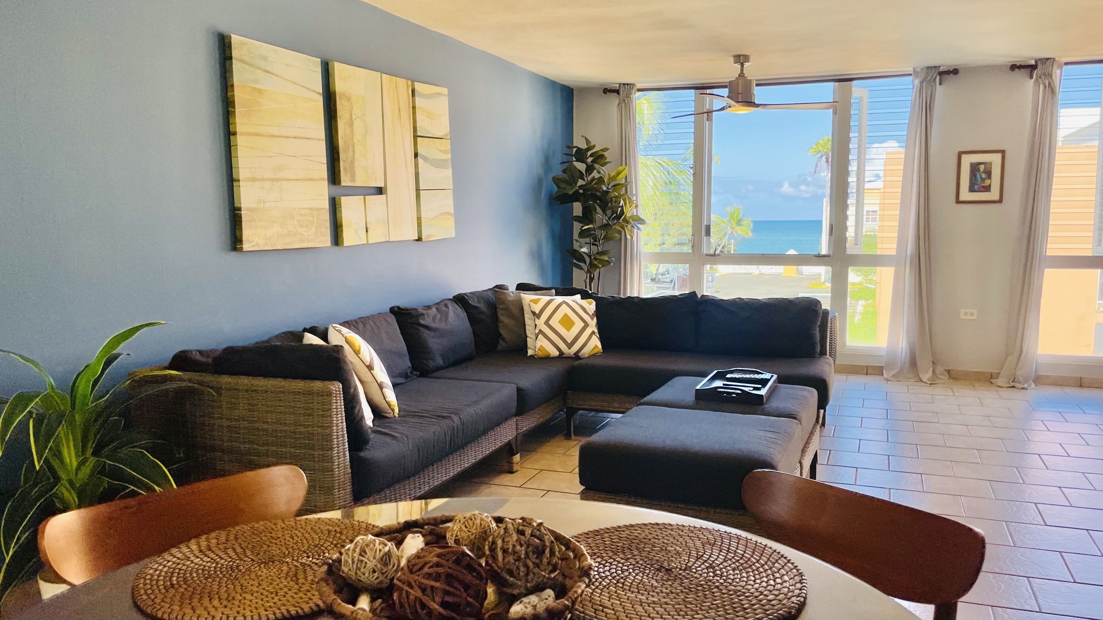 A living room with a sectional sofa, a coffee table, and a large window with a view of the ocean.