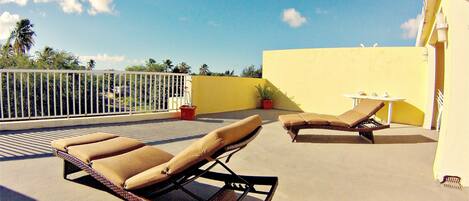 A rooftop terrace with two sun loungers, a small table, and a potted plant.