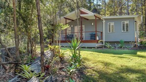 A two-story cabin with a deck, surrounded by a forested area.