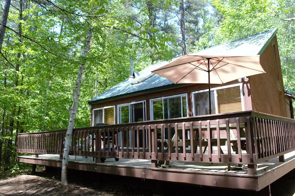 A wooden cabin with a deck, large windows, and a covered patio area.
