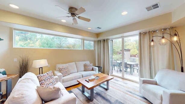 A modern living room with a sofa, armchairs, a coffee table, and a ceiling fan.
