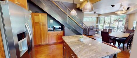 Una cocina moderna con una isla central, electrodomésticos de acero inoxidable y una escalera que conduce a un nivel superior.
