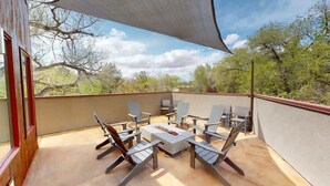 An outdoor patio with a table and chairs, a fire feature, and a view of trees.
