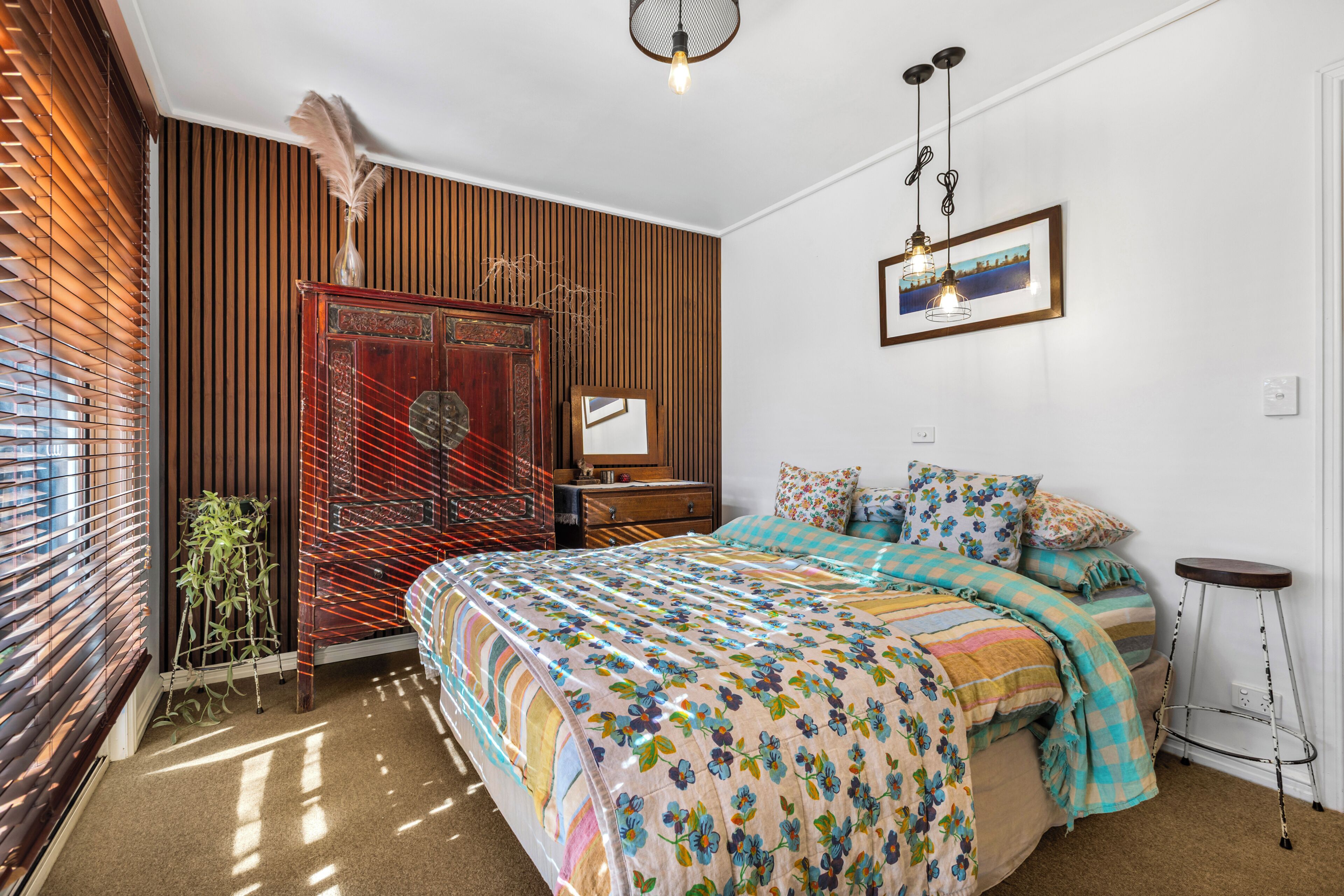 A bedroom with a bed, a dresser, a mirror, a hanging light fixture, and a window with blinds.