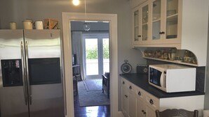 A kitchen with a refrigerator, microwave, cabinets, and a dining area with a table and chairs. - Charming Beachfront Retreat at Bay View – Step Back in Time by the Sea (Flat 2) (Opua)