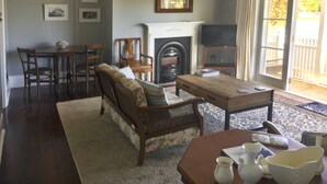 A living room with a fireplace, a sofa, a coffee table, and a television. - Charming Beachfront Retreat at Bay View – Step Back in Time by the Sea (Flat 2) (Opua)