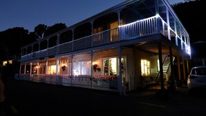 A two-story building with a balcony, a staircase, and a car parked in front. - Charming Beachfront Retreat at Bay View – Step Back in Time by the Sea (Flat 2) (Opua)
