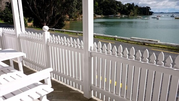 A covered outdoor area with white railings and a view of a lake with boats. - Charming Beachfront Retreat at Bay View – Step Back in Time by the Sea (Flat 2) (Opua)