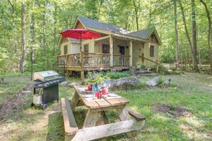 A wooden cabin with a porch, a grill, and picnic table set up outside.