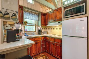 A kitchen with wooden cabinets, a microwave, a refrigerator, and a window with a curtain. - Back on Market! Creekside Studio Near Table Rock (Table Rock)