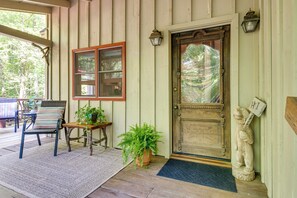 A wooden porch with a door, a window, a chair, a small table, and a potted plant.