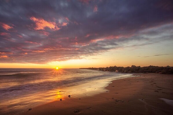 Una playa con atardecer, mar tranquilo y costa rocosa.