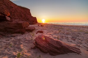 Una playa con formaciones rocosas rojas y un atardecer.