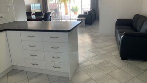 A modern kitchen with white cabinets and a black countertop, a black leather sofa, and a dining area with a table and chairs. - Beachside & Jetty View Apartment 6 ( Captains Apartment)  (Streaky Bay)
