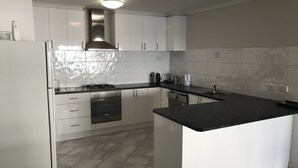 A modern kitchen with white cabinets, a black countertop, and a stainless steel range hood. - Beachside & Jetty View Apartment 6 ( Captains Apartment)  (Streaky Bay)