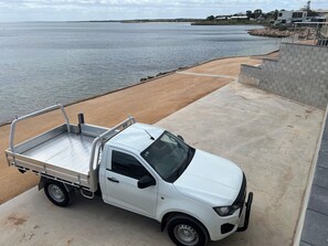 Una camioneta pickup blanca estacionada en un camino de concreto al lado de una playa arenosa y una masa de agua.