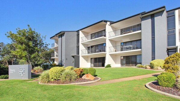 A multi-story apartment building with balconies, a well-maintained lawn, and a utility box labeled "illawong."