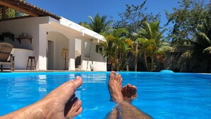 A poolside view with a white building, palm trees, and a clear blue sky. - Pousada Recanto Trancoso (Porto Seguro)