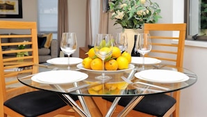 Una mesa redonda de vidrio con platos blancos y copas de vino, rodeada de sillas de madera.
