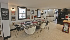 A modern kitchen with a dining area, featuring a large island, white chairs, and various kitchen appliances. - Completely Renovated Historical Home - The Black and White House  (Cape May)