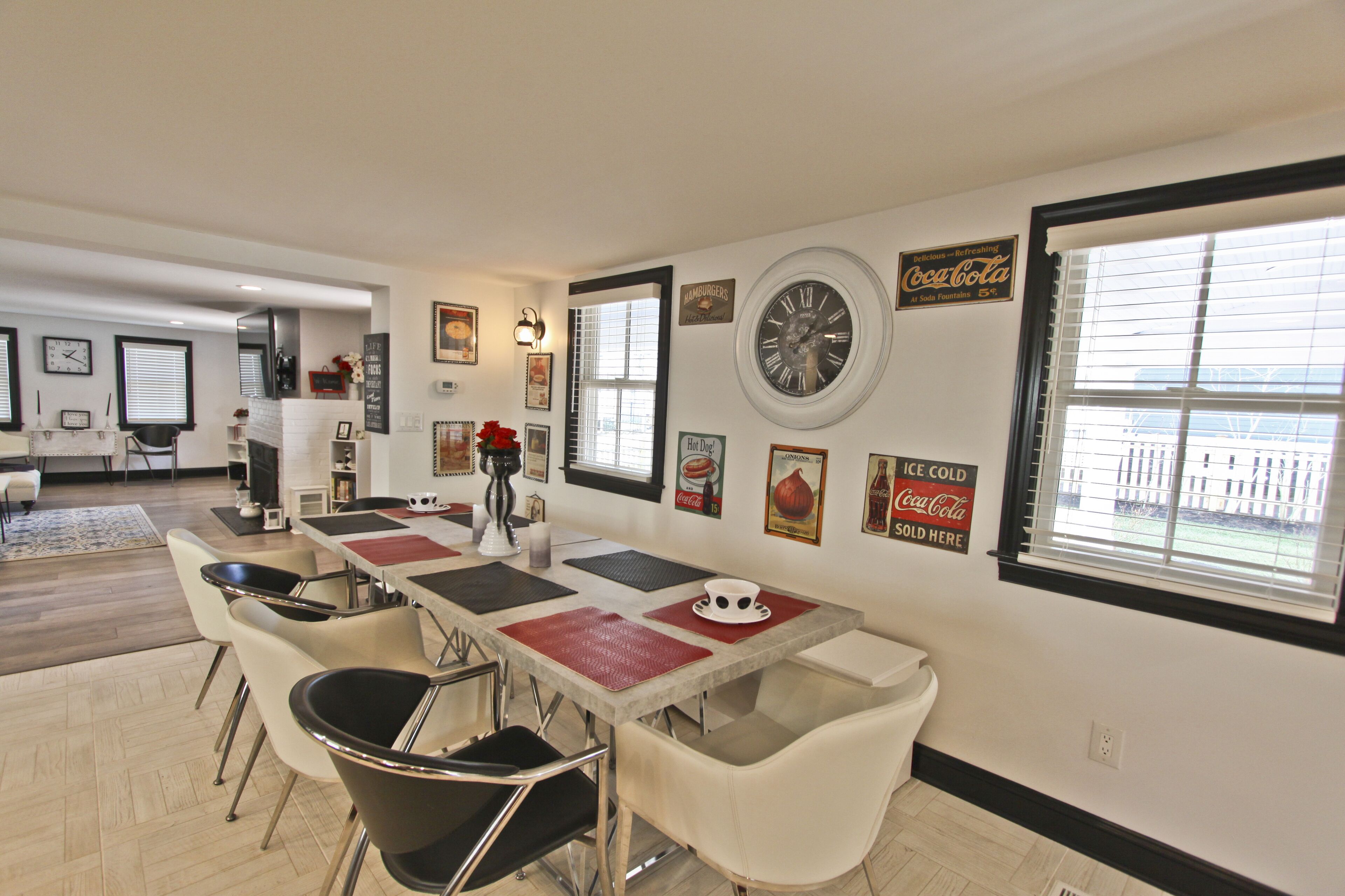 A dining area with a long table, white chairs, and a clock on the wall.