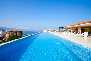A long swimming pool with lounge chairs and a view of the ocean.