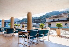 An outdoor patio area with tables and chairs, potted plants, and a view of buildings and mountains.
