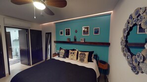 A bedroom with a large bed, a ceiling fan, and a teal accent wall.