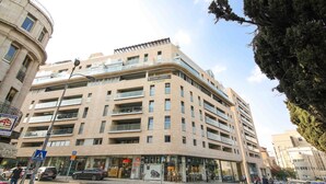 A multi-story hotel with a modern design, featuring balconies and a ground-level retail space.