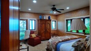 A bedroom with a bed, a red armchair, a wooden wardrobe, and a ceiling fan. - Gated Luxury Lodge - Hot Tub, Mountain Views, Stunning Gardens, Secluded (Franklin)