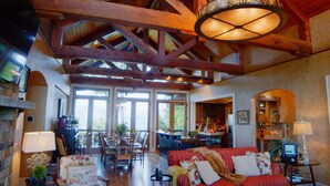 A spacious living room with a high ceiling, wooden beams, a fireplace, and a dining area with chairs and a table. - Gated Luxury Lodge - Hot Tub, Mountain Views, Stunning Gardens, Secluded (Franklin)