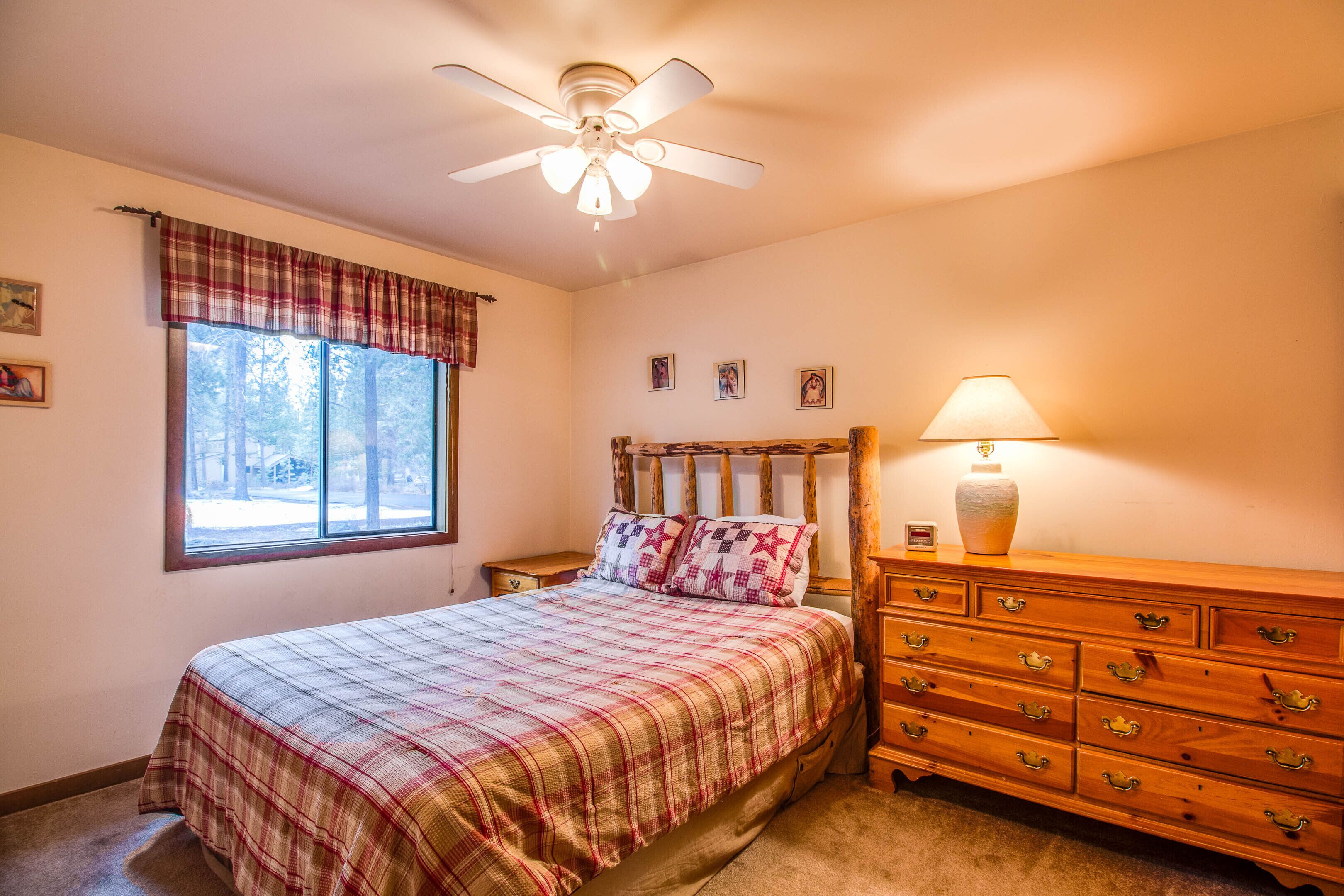 Une chambre à coucher comprenant un lit, une commode, une table de chevet, une fenêtre avec des rideaux, un ventilateur de plafond et une lampe.