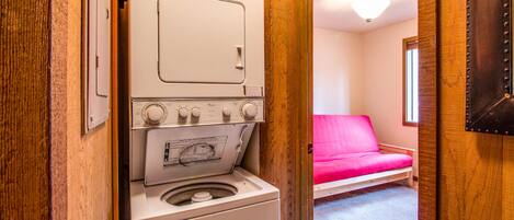 A compact laundry room with a washing machine and dryer, a wooden door, and a pink sofa in the adjacent room.